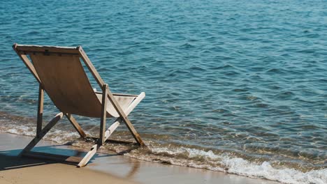 a serene escape: a wooden beach chair reflects tranquility on a calm shoreline with gentle waves lapping at the sand, perfect for relaxation and reflection