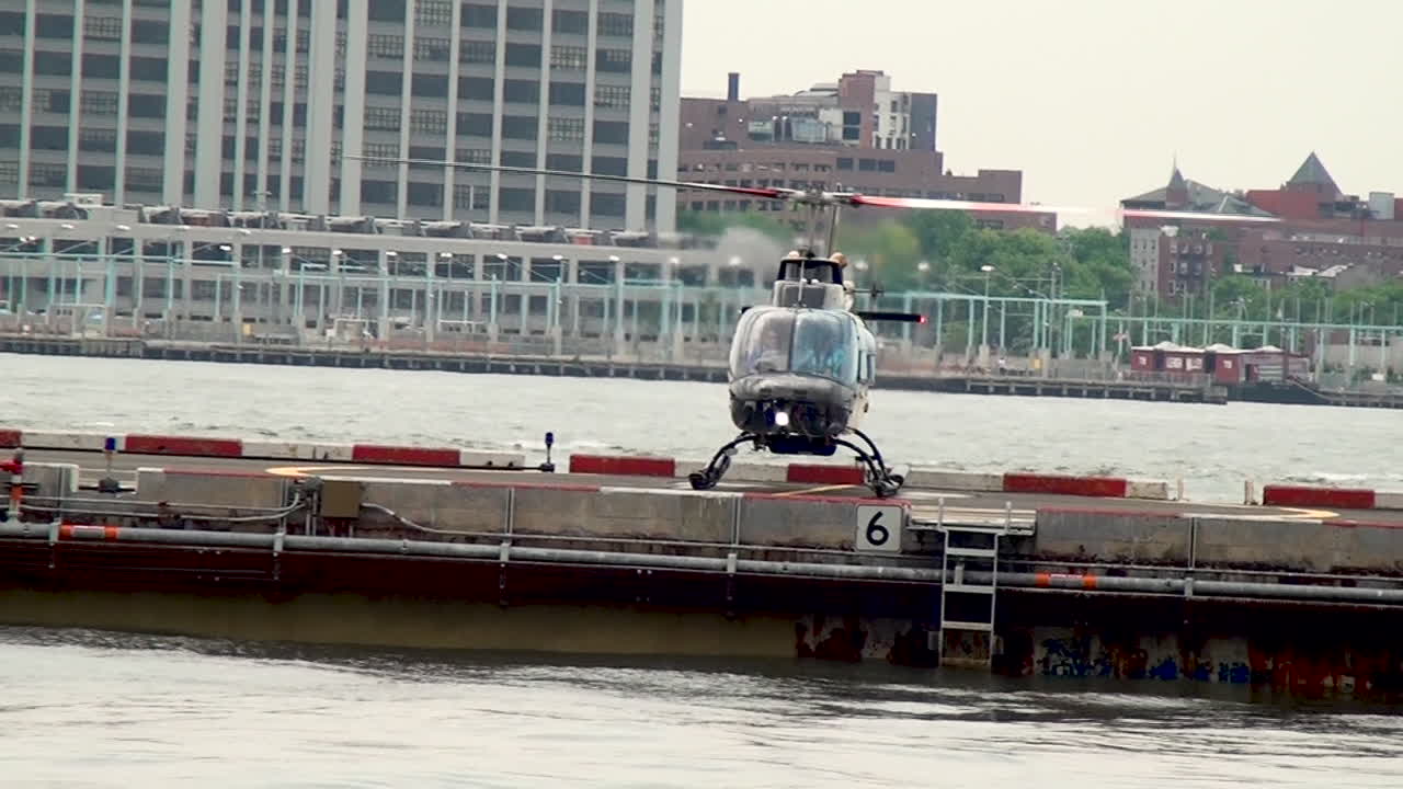 Helicopter lands on heliport pier in Manhattan, Brooklyn skyline is in the background.