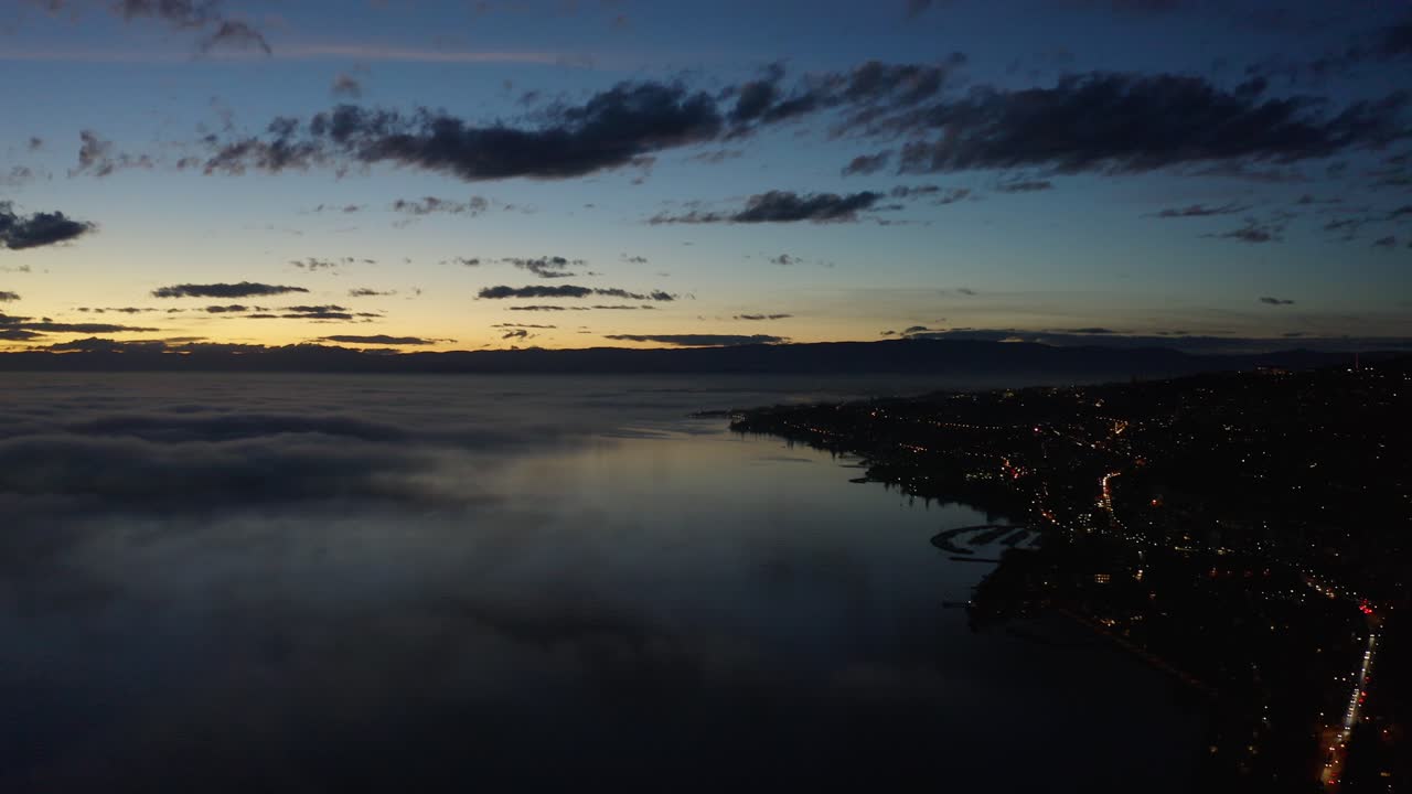 hiperlapso aéreo sobre la orilla del lago léman al atardecer con parches de niebla a baja altura sobre el lago