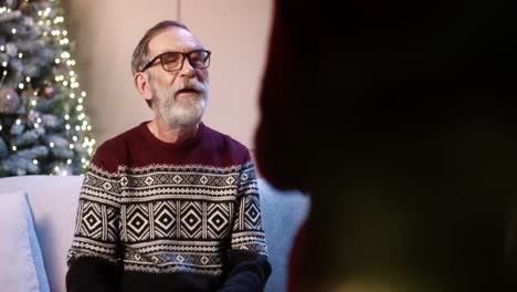 Close-Up-Of-Caring-Teen-Boy-Giving-Xmas-Present-To-Joyful-Old-Grandpa-While-In-Cozy-Decorated-Room-Near-New-Year-Tree