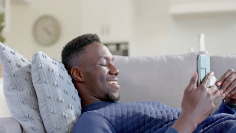 happy african american man using smartphone and credit card in sunny living room, slow motion