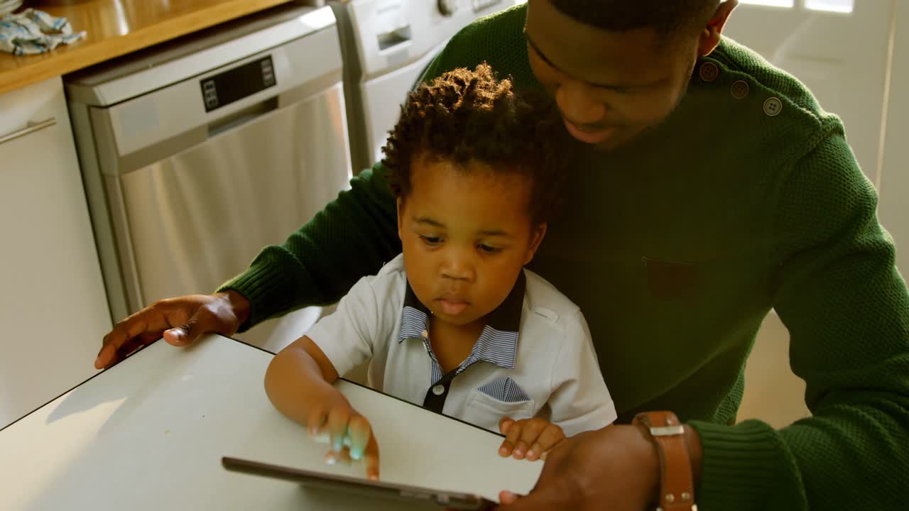High angle view of young black father and son using digital tablet at dining table in kitchen 4k
