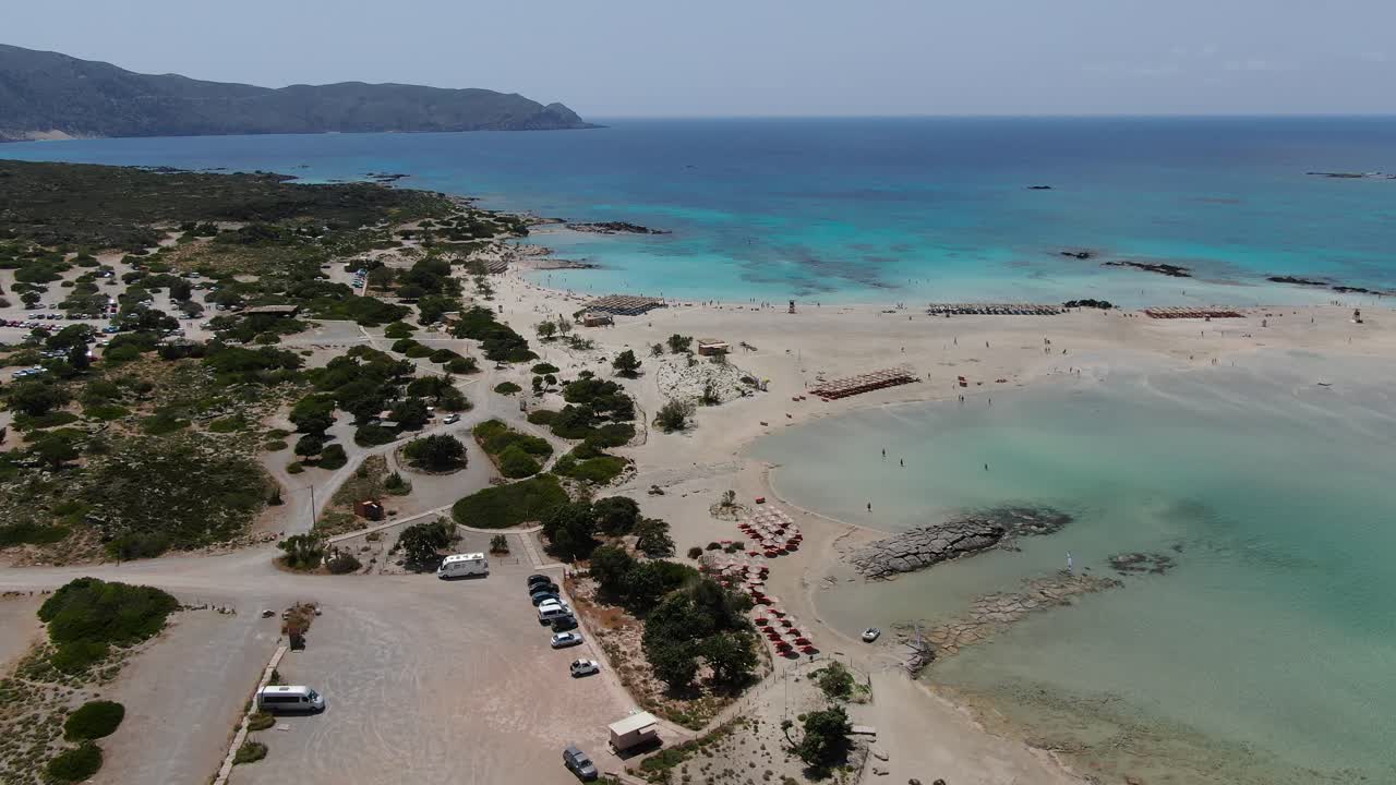 Elafonissi Beach arrival area in Crete Greece with vehicles in the parking lot, Aerial pan left shot