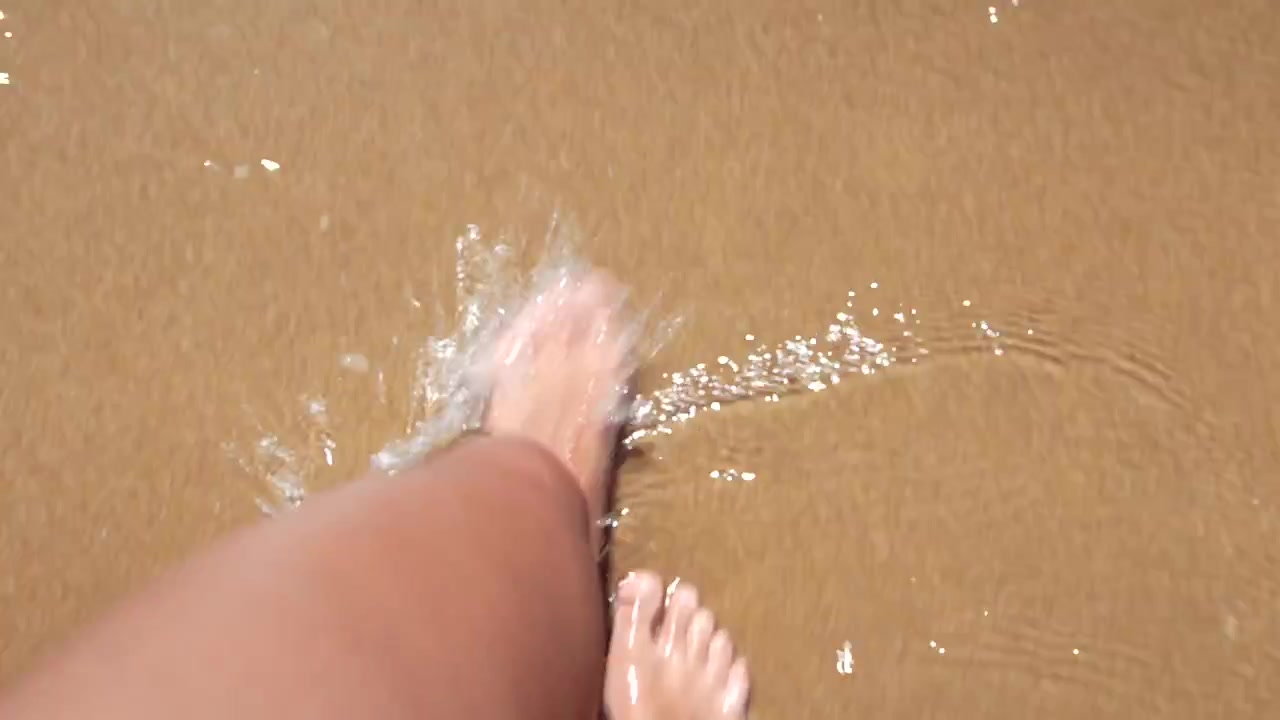 First Person View of Feet Walking in Shallow Ocean Water on Sandy Beach