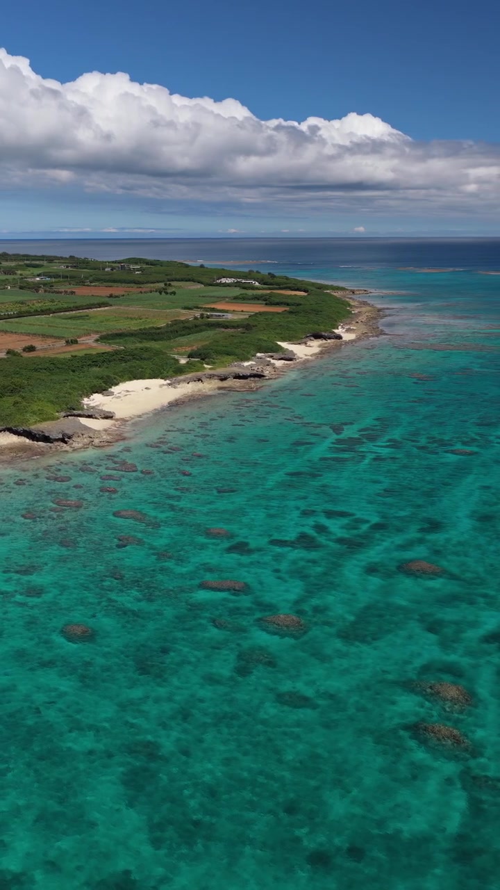 Veduta aerea dei campi agricoli dell'isola di Kurima vicino alla spiaggia di Nagamahama sotto nuvole e cielo blu, Okinawa, Giappone