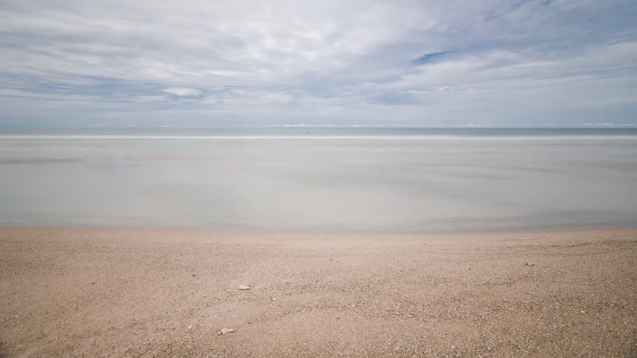 햇빛이 비치는 낮에 평화로운 바다에서 하얀 모래와 파도가 있는 시간 경과