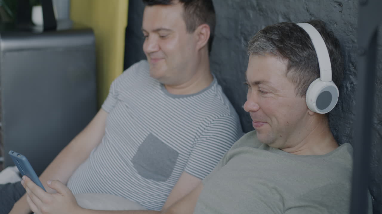 Two men relaxing at home, using technology and listening to music