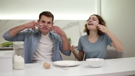 pareja positiva linda manchas de harina en sus caras en la cocina. feliz pareja joven tonteando mientras cocina la comida. cámara lenta