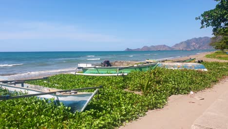 Coloridas-Canoas-De-Pesca-De-Madera-Tradicionales-Asiáticas-Alineadas-A-Lo-Largo-De-La-Costa-Con-Olas-Oceánicas-Rodando-En-Un-Día-Soleado-Y-Azul-En-La-Capital-Dili,-Timor-Leste,-Sudeste-Asiático