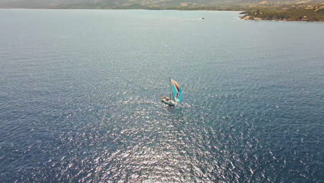 sailboat with colorful sails sailing in mediterranean sea by a coast of sardinia island, italy, drone aerial view