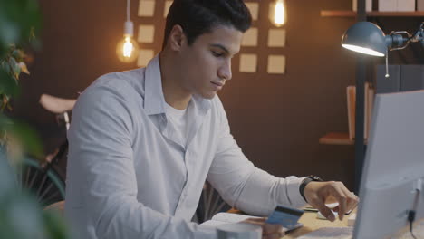 young man working on a computer and using credit card