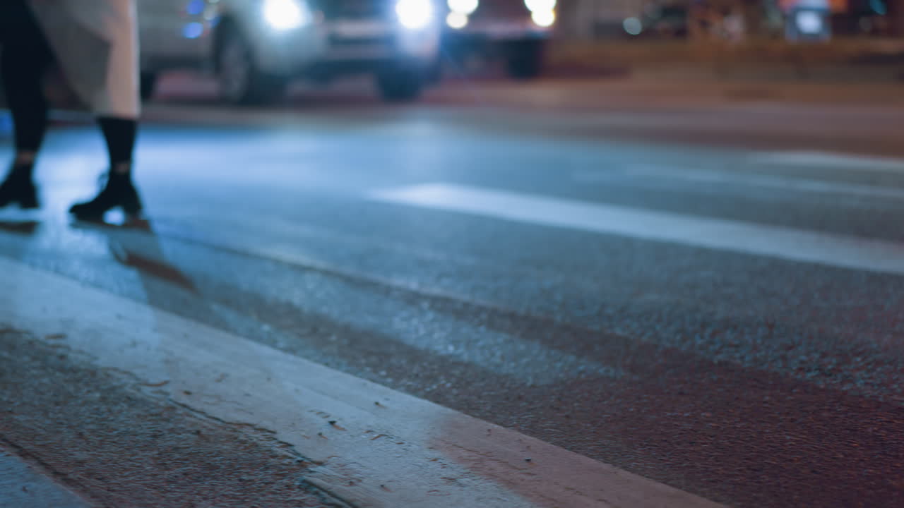 교통 신호등에서 기다리는 자동차와 함께 밤에 거리를 가로지르는 사람의 가까운 시각