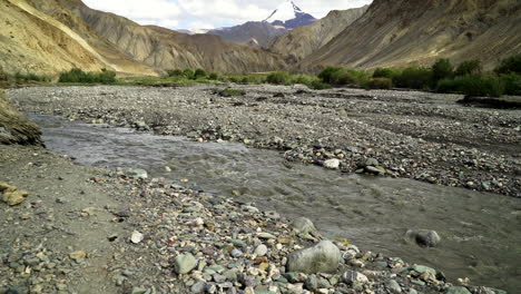 tilt down shot from the high snowy mountain peak to a tiny river flows on a rock bed