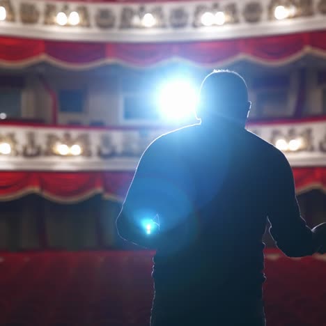 Speaker on stage against bright spotlight. Back view of an actor man during the rehearsal in the classical theater