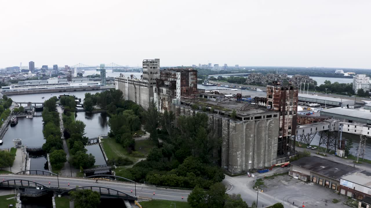 Aerial view of rusted industrial silos with a modern city skyline backdrop. A stunning contrast of urban decay and sleek architecture. Montreal's Old Port docks.