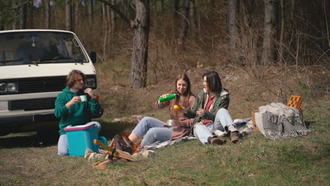 two young girls and a young boy have a good time in the forest having a hot beverage