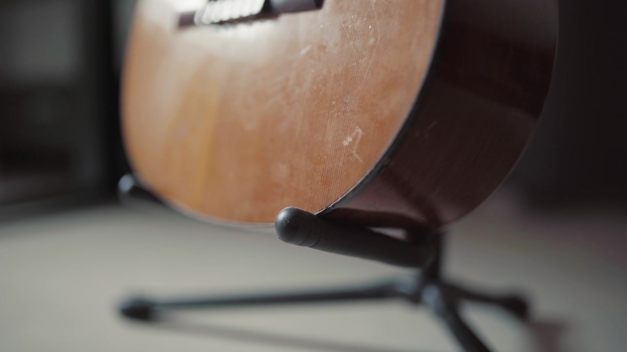 Chitarra acustica appoggiata su un supporto in luce soffusa con sfondo sfocato, ambiente caldo e tranquillo