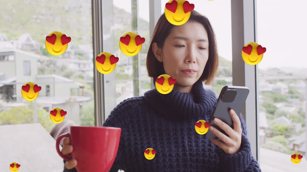 Animation of emoji icons over asian woman drinking coffee and using smartphone at home