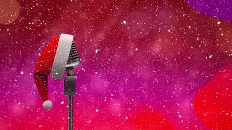 Snow-falling-over-microphone-with-Santa-hat-against-glowing-spots-on-purple-background