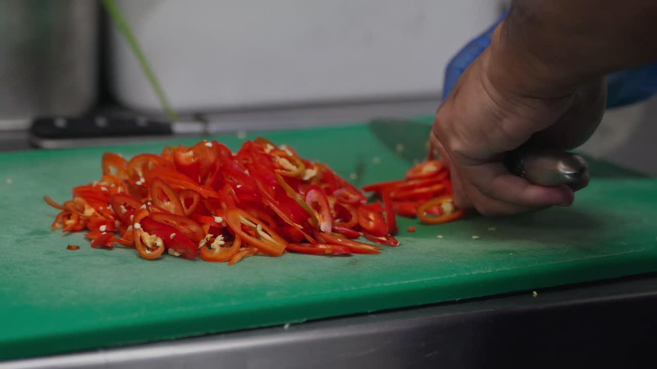 Close up, A chef slicing red spicy chilli’s on a green chopping board in a commercial kitchen