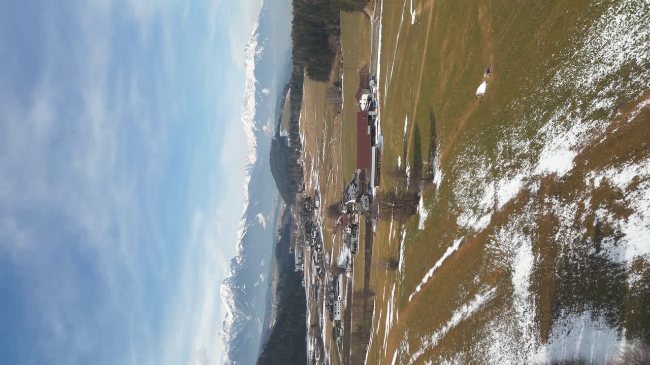 vídeo vertical: vista aérea por drones de campos marrones con pequeñas partes cubiertas de nieve y caminos con bosques y casas