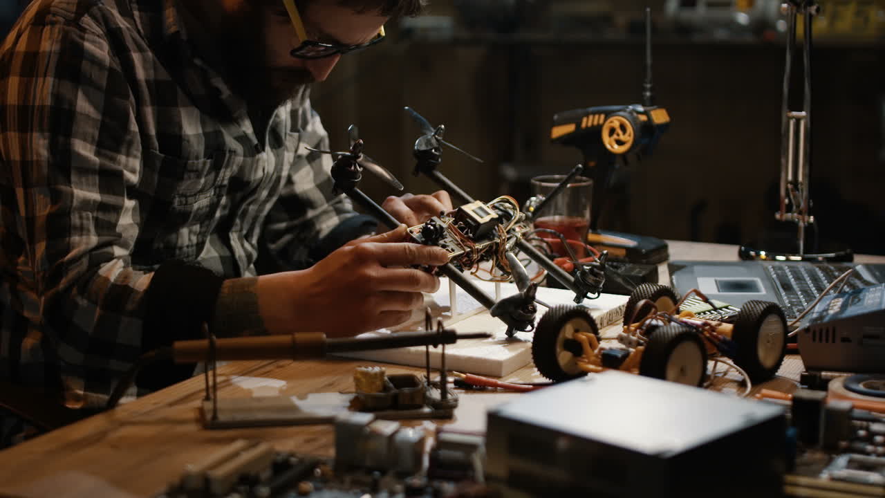 Person repairing a drone and a remote-control car in a workshop.