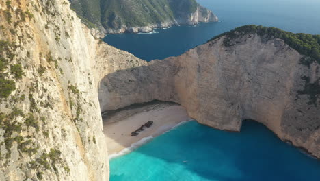 Atemberaubende-Drohnenaufnahmen-Vom-Schiffswrackstrand-Am-Navagio-Strand,-Umgeben-Von-Hohen-Klippen-Und-Klarem-Blauen-Wasser