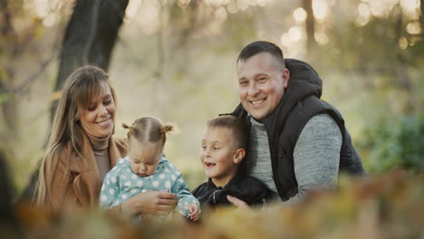 portrait of a young family with two children - a boy and a girl. sitting in the autumn park, looking at the camera