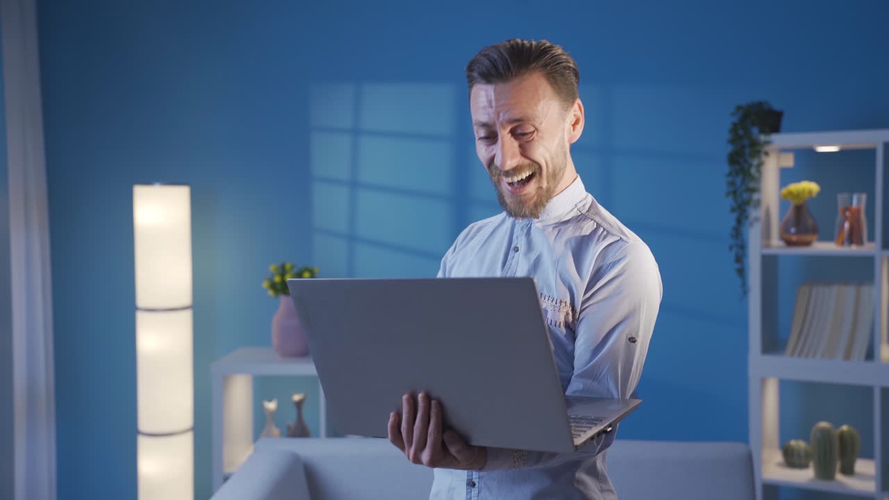 hombre feliz y elegante trabajando remotamente en una computadora portátil mientras baila y se divierte en casa.