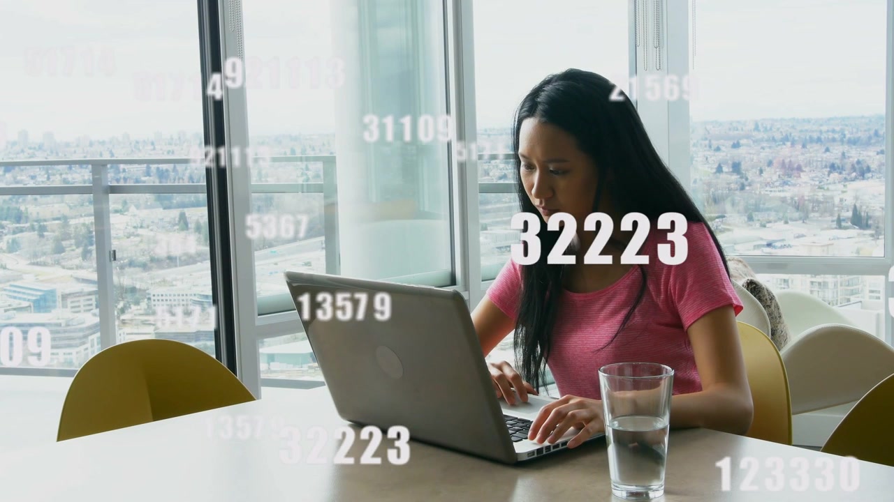 Donna che digita al laptop in un grattacielo, con numeri che appaiono a sinistra e la portano a chinarsi per l'analisi dei dati.