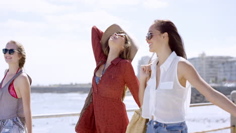 Three-young-women-tourists-on-summer-vacation-walking-on-beach-promenade-looking-up-at-sky