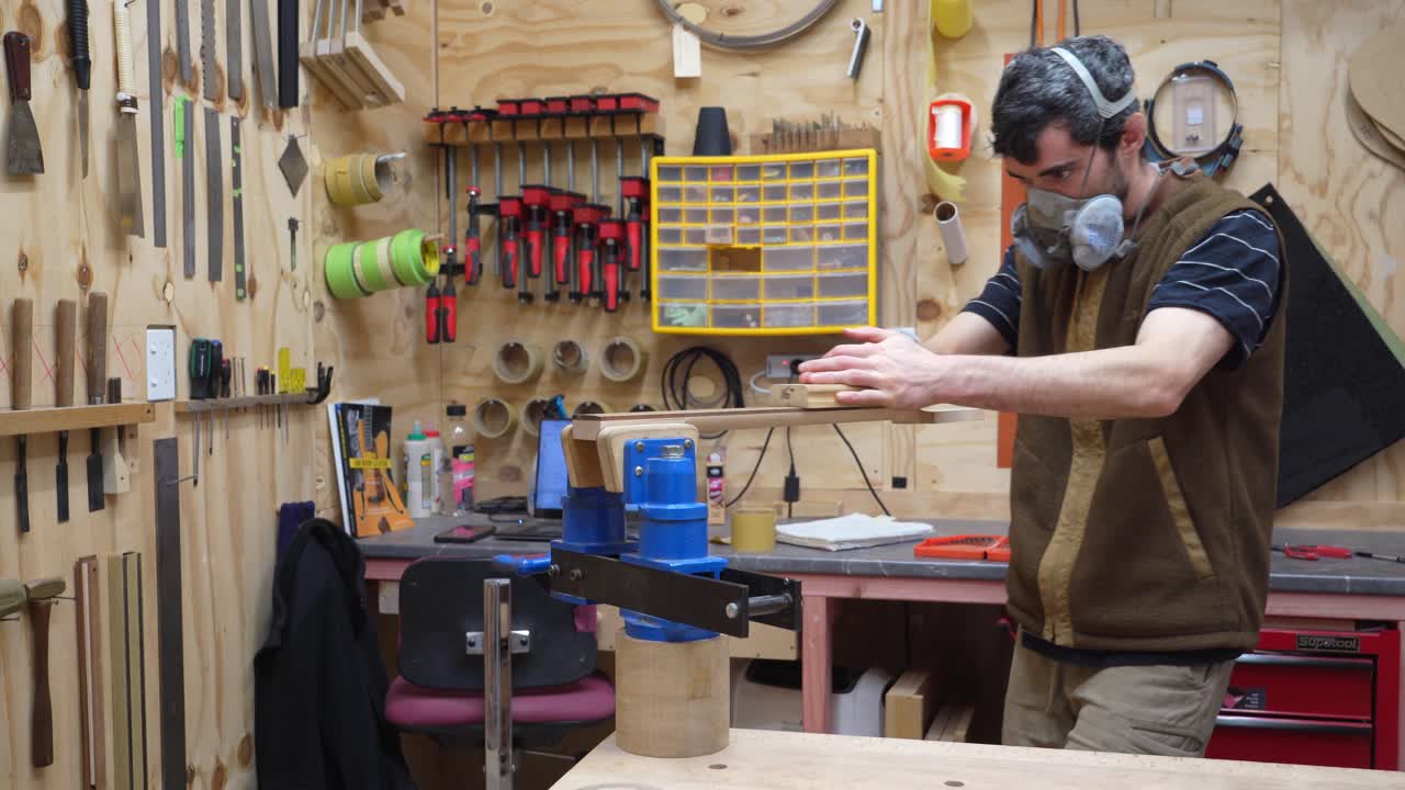 luthier de guitarra con máscara protectora que termina el diapasón de la guitarra con papel de lija de grano fino, radio de lijado del diapasón en el taller