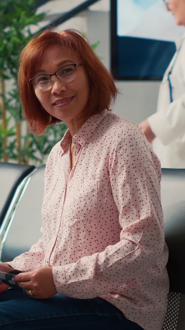 Vertical video: Portrait of asian elderly patient waiting in hospital lobby