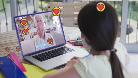 Animation-of-heart-icons-over-girl-in-face-mask-using-laptop-on-video-call