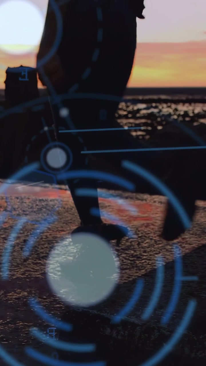 Video verticale: Donna che cammina su una costa rocciosa al tramonto, entrando e oscurando un test tecnologico HUD.