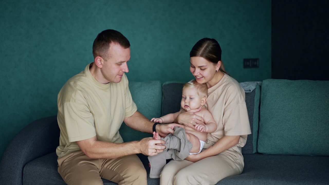 Caring parents are dressing their beloved baby. Father is putting on the pants on his cute son.