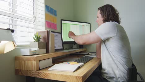hombre caucásico enfocado trabajando remotamente, usando computadora portátil y hablando en teléfono inteligente