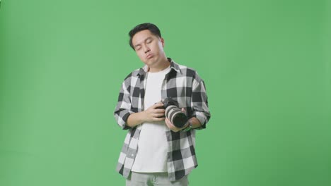 asian photographer having a neck ache after using a camera taking some pictures while standing on green screen background in the studio