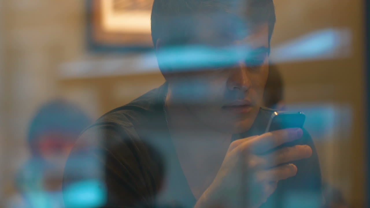 Young man behind the glass texting on smartphone