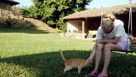 Katzenliebhaber,-Der-Auf-Einer-Gartenschaukel-Sitzt,-Streichelt-Und-Kuschelt-Die-Süße-Ingwerkatze