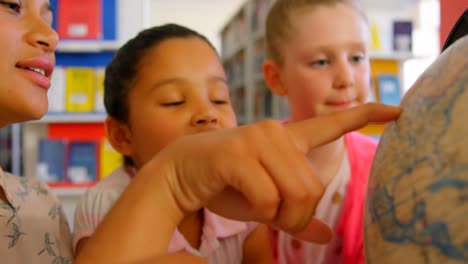 maestra asiática enseñando a los niños sobre el globo en la mesa en la biblioteca de la escuela 4k