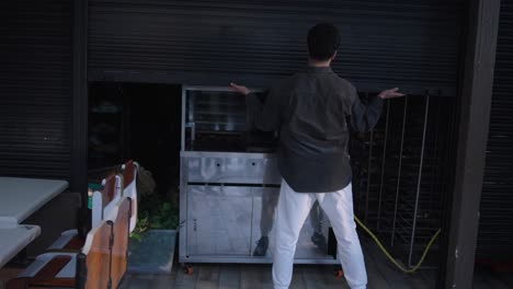 baker opening bakery shop and pulls up the blind with his hands with morning light shining.