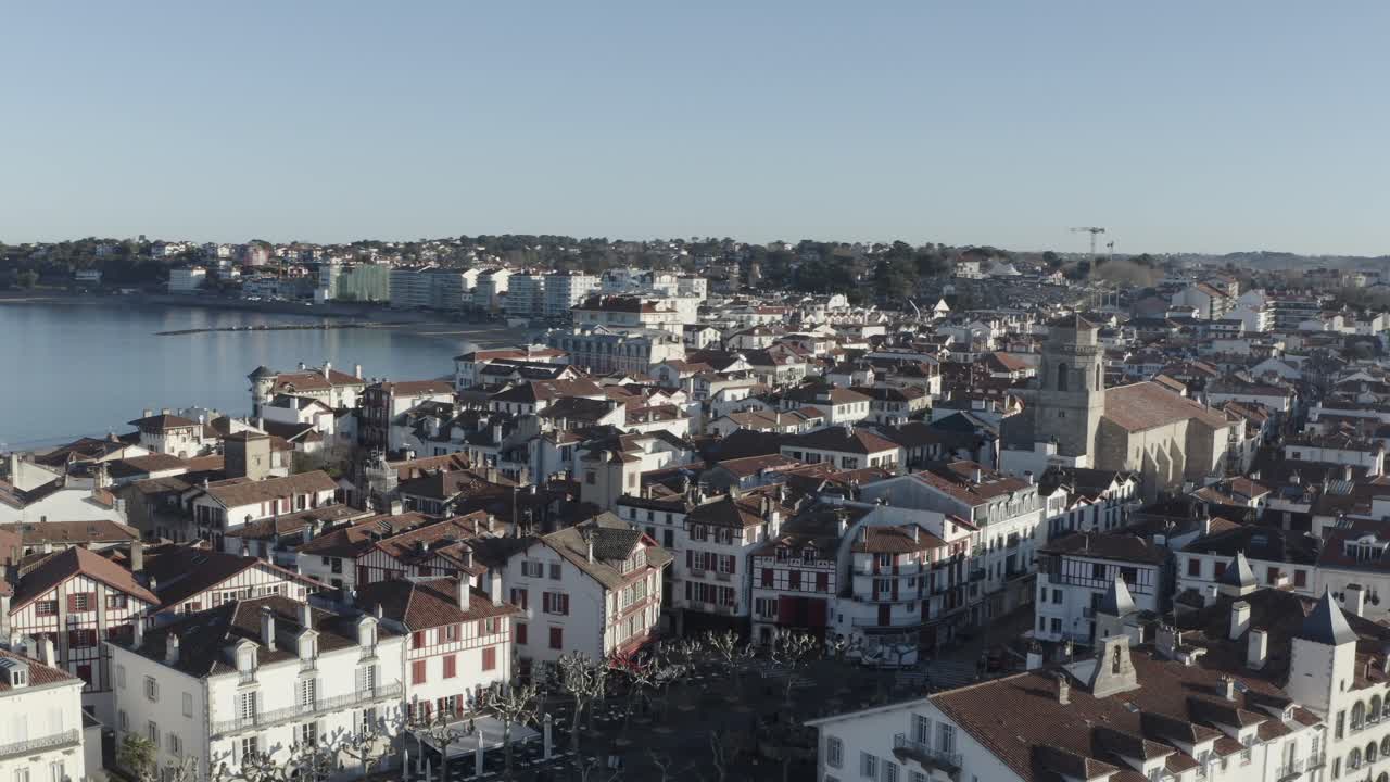 Historic Saint-Jean-de-Luz, traditional Basque architecture, rooftops, church tower, calm bay, sunny day, France. Aerial drone panoramic view, copy space