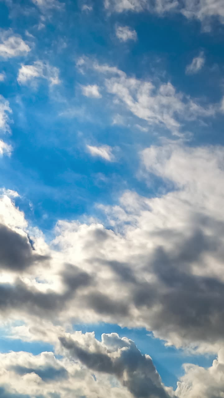 Sun beaming through the clouds moving along the bright summer sky. Skyline clears away. Timelapse. Vertical video