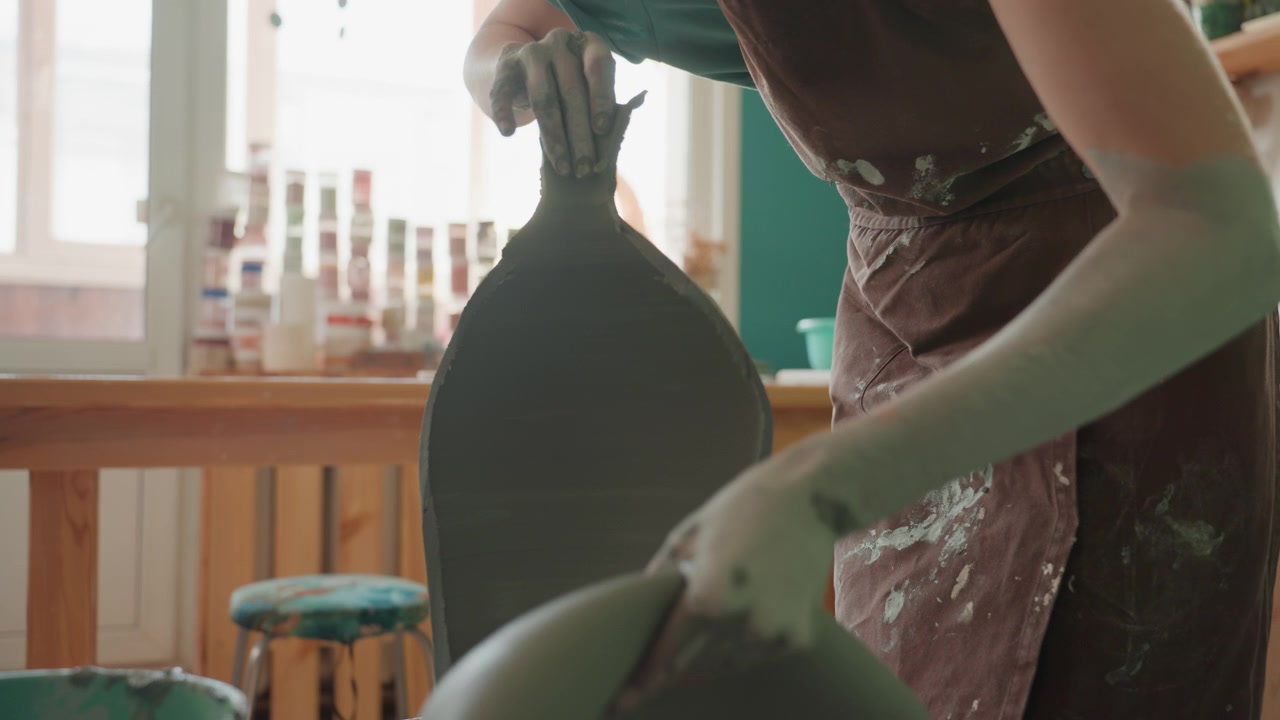 Ceramista donna bianca che rifinisce con precisione il bordo di un vaso al tornio in un laboratorio luminoso, primo piano di mani e strumento che levigano la silhouette, finitura e controllo concentrati, atmosfera tattile dello studio.