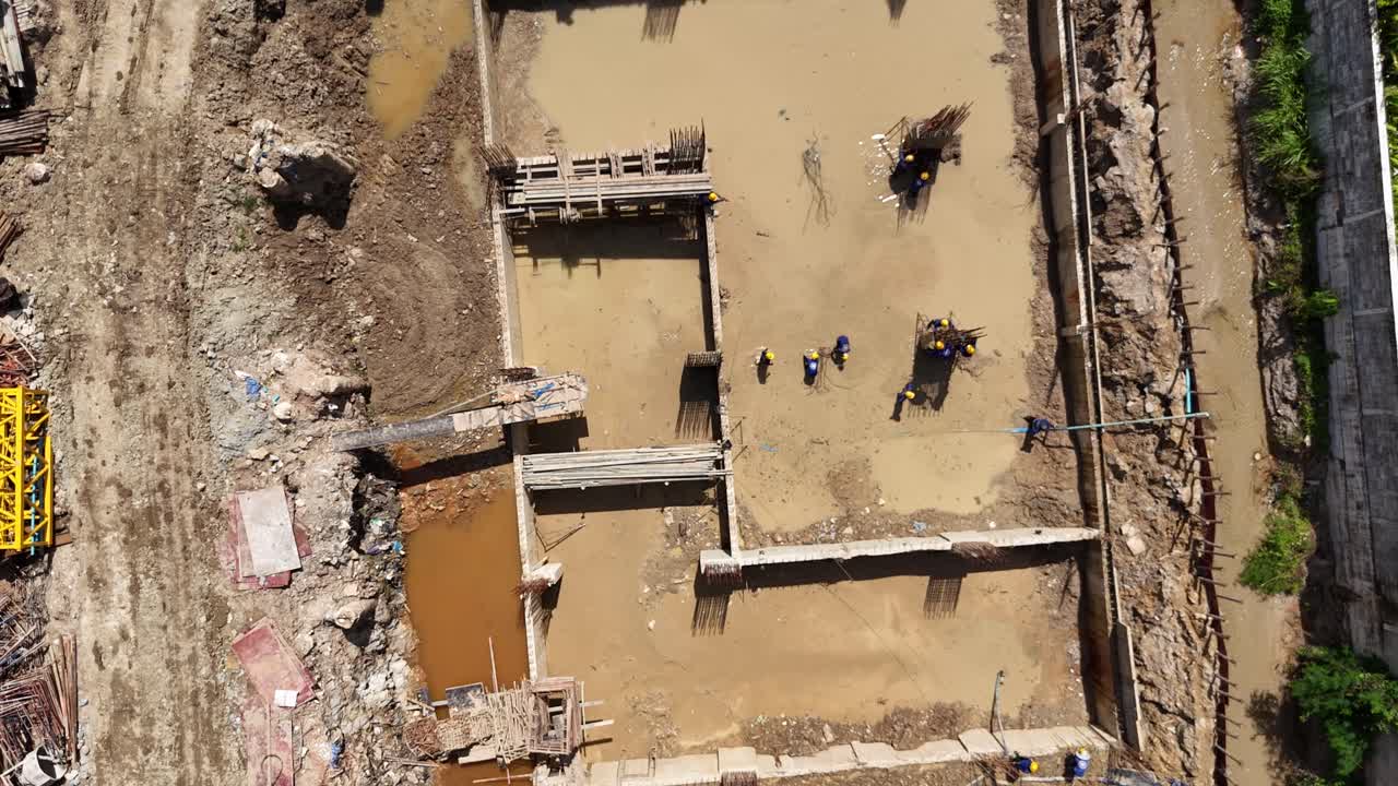 Aerial view of a construction site with workers building a foundation next to a completed building with a pool