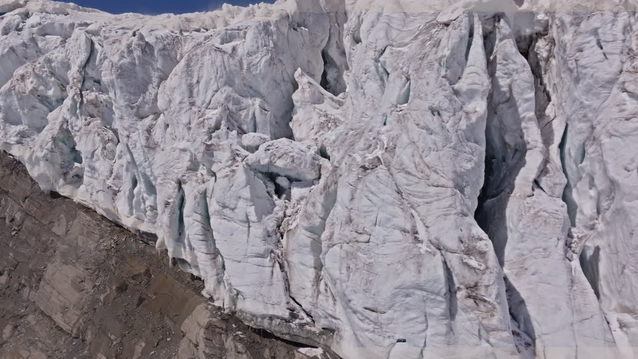 A powerful drone shot revealing massive overhanging seracs and towering ice cliffs in Saas-Fee, Switzerland. The frozen formations glisten under alpine light, showcasing the raw power of the glacier
