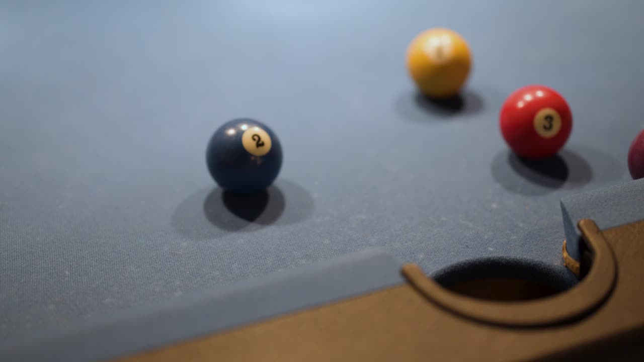 Yellow pool ball narrowly misses pocket, rolling past blue and red balls on dim table