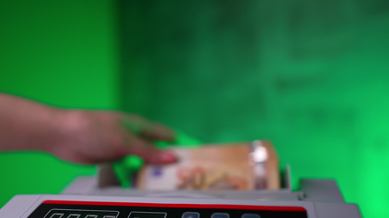 Female cashier's hand places money into cash counting machine. Fifty euro stack is quickly counted in device. Close up.