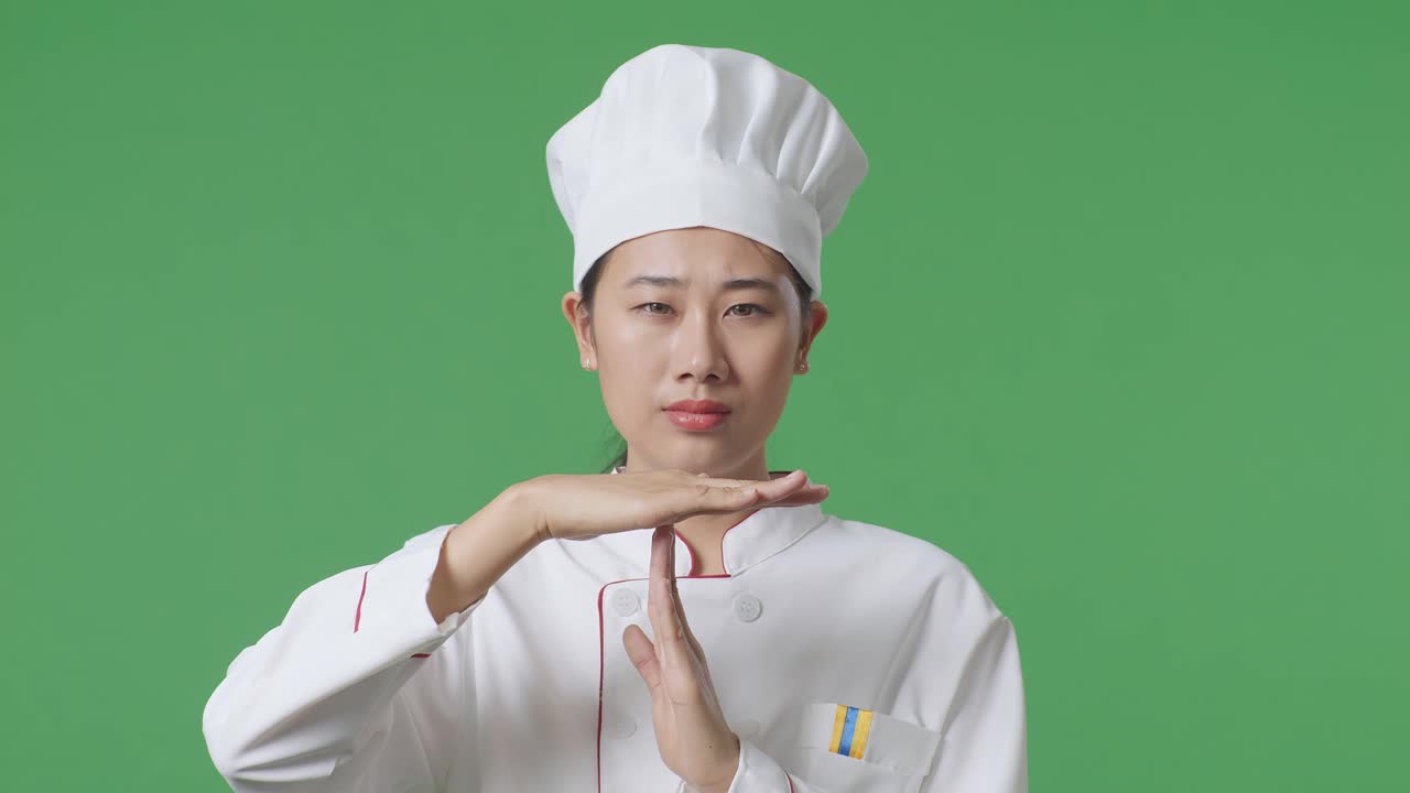 Close Up Of Asian Woman Chef Looking At Camera And Showing Time Out Hands Gesture While Standing In The Green Screen Background Studio